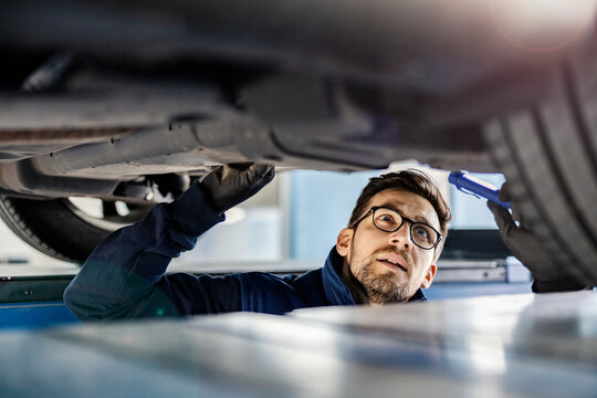 A Focused Auto Mechanic In Mechanic's Pit Looking At Malfunction On Car.