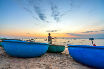 View of the beach at the basket boat dock at sunset as the fishermen are at their nets preparing to set sail the next morning in Mui Ne, Vietnam