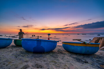 View of the beach at the basket boat dock at sunset as the fishermen are at their nets preparing to set sail the next morning in Mui Ne, Vietnam