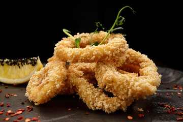 Fried onion rings in batter, on a black plate, on a black background