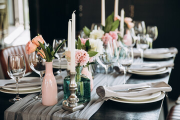 Wedding. Banquet. Decor. Festive tables are decorated with fabric, compositions of flowers and greenery in glass vases, there are candles, glasses, plates and cutlery on the tables