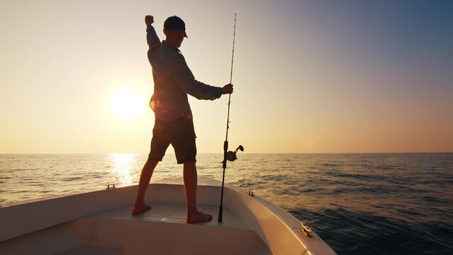 Open sea fishing. Angler stands with fishing rod on the boat floating in the open sea and looks somewhere