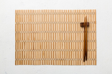 Two chopsticks and bamboo mat on cement background. Top view, copy space