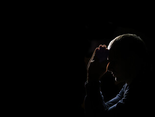 Young man praying on dark background - obrazy, fototapety, plakaty