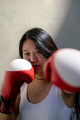 Chinese woman with tough look training with red and white kick boxing gloves looking at camera