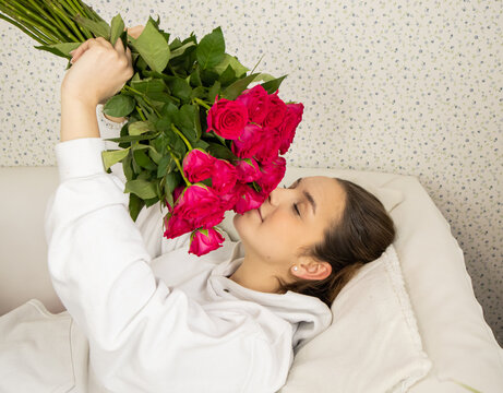 The young and happy girl lies on the bed and smells the roses, closing her eyes. Concept holiday, wedding, birthday, surprise High quality photo