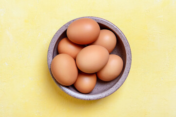 Fresh farm chicken eggs in a bowl on a yellow background. Top view.