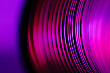 Closeup of coiled metal spring rings in a compressed state in pink and blue neon light. Macro...