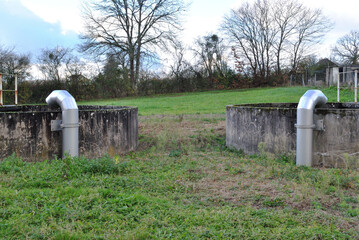 Old Concrete Storage Tanks and Modern Metal Pipes in Rural Field with Autumn Trees