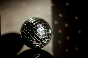 Disco ball reflects light in room. Ball of small mirrors stands on surface of speaker.