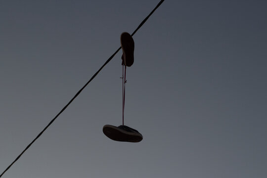Sneakers hang on wire. Shoes hang on shoelaces on electrical wire. Boots against sky.