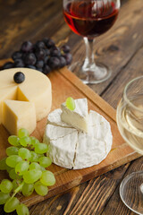 Various types of cheese with dark and green grapes and wine on wooden table.