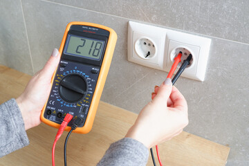 Woman with a multimeter check the voltage of the electrical network. woman checking voltage in...