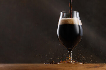 Stream of dark stout pours into a beer glass. Detail of dark beer with overflowing foam head and drips. Selective focus	