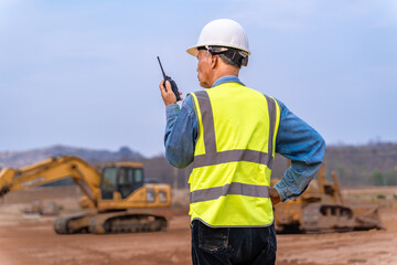 Senior supervisor engineer in his work cloths communicating to his working staff through walkie talkie at construction site