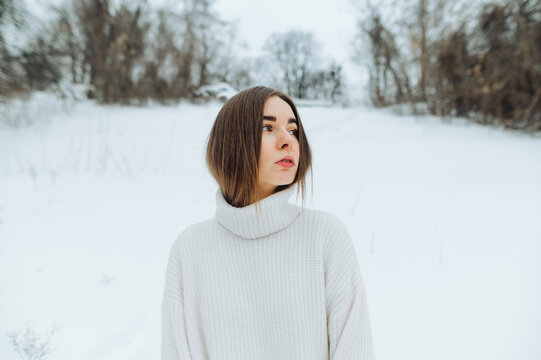 Portrait of a beautiful woman in a sweater standing on the street in winter and looking away with a serious face.