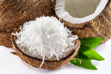 Cracked coconut fruit with white flesh and shredded coconut flakes isolated on white background.