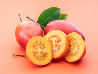 Ripe tamarillo fruits with slices and tamarillo leaves isolated on a orange background.