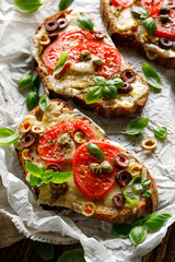 Grilled open faced sandwiches made of sourdough bread with the addition of cheese,  tomatoes and olives sprinkled with fresh basil on a wooden board, close up view