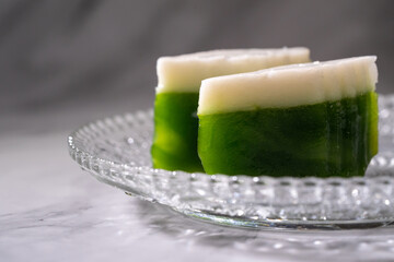 Nyonya delights dessert “Kuih Talam” (Pandan Tray Cake) on white plate and isolated marble...
