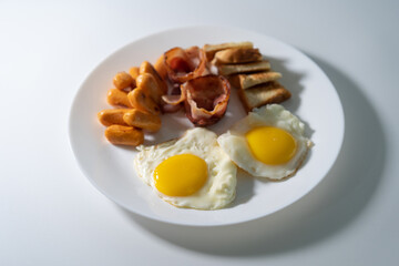 Western brekfast on isolated white background. Sunny side up eggs, sausage, vacom and toast bread.