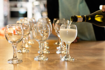 Pouring white wine from bottle into the wineglass on the table over blurred background