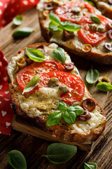 Close up view of toasted sandwich from traditional sourdough bread with cheese, tomatoes, olives and capers sprinkled with herbs on a wooden board
