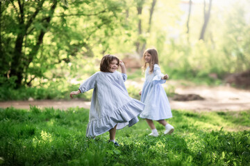 Happy funny children are spinning in the meadow in the park, girls in beautiful dresses hold hands and play in the tall grass. Happy childhood and spring.