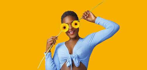 Portrait of a happy young woman holding yellow Gerbera daisy covering her eye with eyes closed 