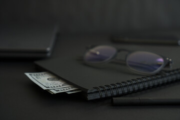 On a black background: Money, notepad, laptop, glasses.