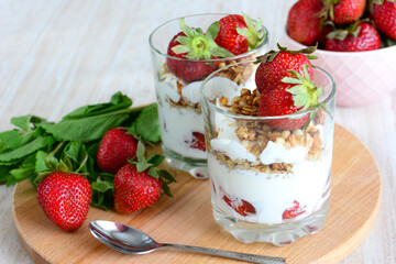 granola with yoghurt in glasses decorated with strawberry, closeup