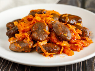 Stewed broad beans in tomato sauce with vegetables and spices close-up on the wooden table. Faba beans with carrot, onion and tomato. Side view, close up.