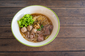 Beef noodles with braised beef, liver, and meatball are delicious food in Thailand. Chinese-style on the old wooden table.