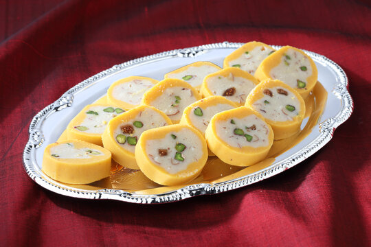 Pedha Indian traditional sweet made of milk served in a silver decorative plate on red silk cloth background