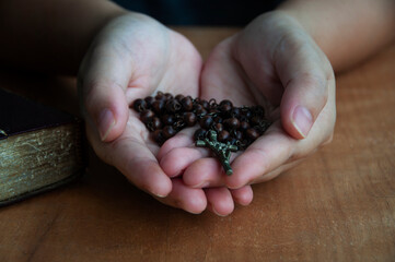 Hand holding Holy Rosary with wooden table background. Religious concept