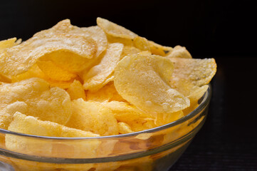Crispy potato chips in white bowl with black background