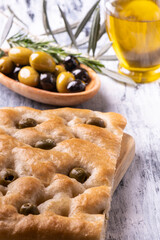 in the foreground tasty Genoese focaccia with olives, in the background cruet and olives.