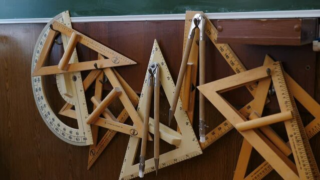 Set of big rulers. compasses and protractors hanging in classroom. School blackboard kit for drawing. Various tools for technical drawing in mess, Male hand hanging one item of school stationary
