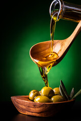 from the wooden spoon, in the foreground, the extra virgin olive oil is poured into an olive wood...