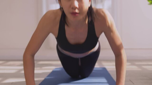 Asian woman in sportswear doing push ups workout exercise on exercise mats at home in the morning.