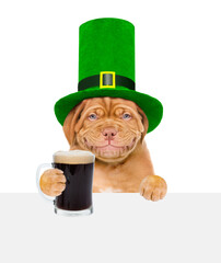 St. Patricks Day. Funny puppy wearing hat of the leprechaun holds dark beer above empty white...