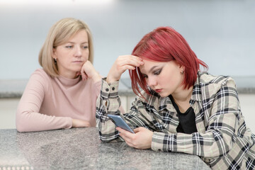 Unhappy mother looks at her teenage daughter, girl uses smartphone and ignores her mom. Family relationships