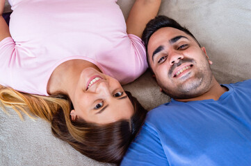 top view of heterosexual couple together lying on bed looking at camera and smiling