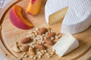Camembert Cheese on a wooden board with almonds, cashews, pine nuts and peach. Serve french homemade soft cheese. Selective focus on a piece of cheese