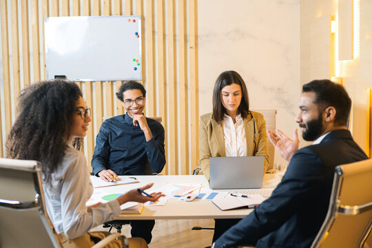 Multiracial team. Group of ambitious young people in smart casual wear discussing business tasks while sitting at the table in a modern office. Flip chart on the background