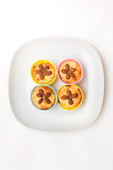 Close-up of homemade vanilla cakes with whole almonds in multicolored silicone cups on a white plate. Healthy snack.