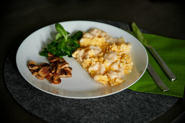 Beautiful breakfast in a white plate on a black table. Omelet with cheese, mushrooms and spinach on a white plate. Eggs with cheese. Beautiful breakfast service. A green napkin lies near the plate.