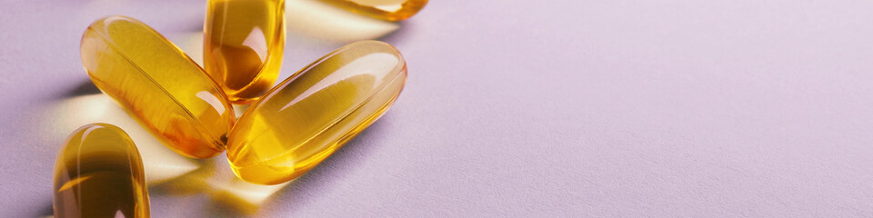 Fish oil. Yellow softgels or capsules lie on a pink surface. Vitamins and a healthy lifestyle. Banner or headline. Softgel close-up. Omega-3 fatty acids. Macro
