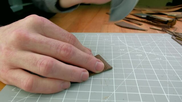 Close up hands tanner cuts special halberd cutting knife leather piece in workshop. Craft production.
