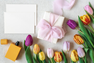 Colorful spring mockup of bright tulips, perfume, and card on a neutral background.